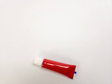 Yakın plan bir fotoğraf temiz beyaz bir yüzeyde duran tek bir krem ya da merhem tüpünü gösteriyor. Tüpün konumu bir açıda, beyaz başlık ve sıkıştırılmış ucu görünür durumda. Işıklandırma parlak ve pürüzsüz dokuyu vurguluyor.