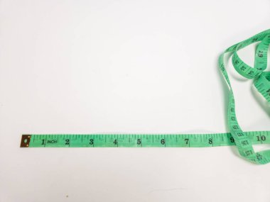 Yeşil bir ölçüm bandının yakın çekim görüntüsü beyaz bir arkaplan boyunca çaprazlamasına uzanır. Bant hem santimetre hem de santimetre ile işaretlenmiş ve kısmen kıvrılmış. Arkaplan sade ve temiz, bu da bandı resmin odak noktası yapıyor.