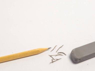 Yakın plan çekimde beyaz bir yüzeyde sarı bir kalem ve gri bir silgi görülüyor. Kalem kırıntıları silginin yanına saçılmış. Düzeltme ya da düzenleme anlamına geliyor. Kompozisyon, yazı, çizim ve yaratıcı halkla ilişkilerde kullanılan kırtasiye malzemelerine odaklanır.