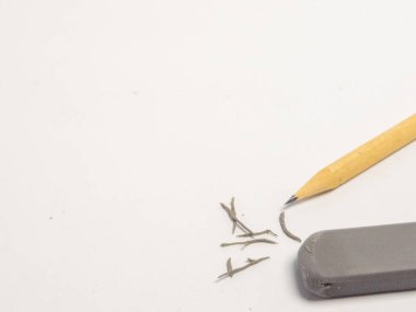 Bir yakın çekim beyaz bir yüzey üzerinde bir kalem ve silgi içerir, kalem talaşı etrafa saçılmıştır. Kompozisyonda yazma ve silme, yaratıcılık, eğitim ve revizyon sürecini önerme araçları vurgulanıyor. Yumuşak ışık...