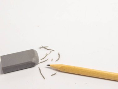 Gri bir silginin yakın çekimi, sivri bir tahta kalem ve beyaz bir yüzeye saçılmış silgi talaşları. Görüntü düzeltme, hatalar, öğrenme ve eğitim kavramlarını aktarır. Kompozisyon basit ve temiz, objec 'e odaklı.