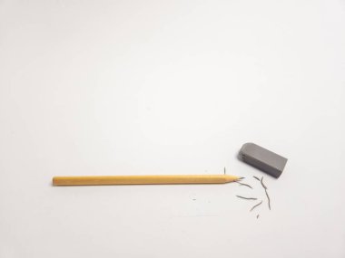 Ahşap bir kalem ve temiz beyaz arka planda gri bir silginin yer aldığı yakın çekim bir stüdyo resmi. Kalemin ucu, yakınlara saçılmış silgi talaşlarıyla kullanım belirtileri gösteriyor. Bu da hataları düzeltme, düzeltme ve düzenleme sürecini sembolize ediyor. Ödeme.