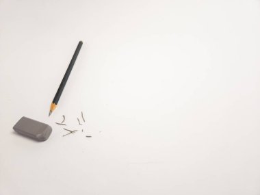 Keskinleştirilmiş bir kalem ve beyaz bir yüzey üzerinde gri bir silginin yer aldığı basit bir natürmort yaşam formu. Sahne, hataları silme ve düzeltme eylemini görsel olarak temsil eden kalem talaşı içeriyor. Görüntü basitlik duygusunu iletir, cl
