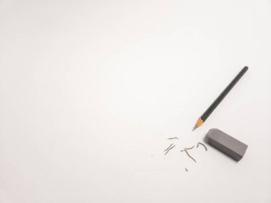 Keskinleştirilmiş bir kalem, dikdörtgen bir silgi ve temiz, beyaz bir arkaplanda kalem talaşı içeren durgun bir yaşam görüntüsü. Kompozisyon basit ve minimalist, yazma ve çizim için kullanılan araçları vurguluyor. Görüntü iyi aydınlatılmış.