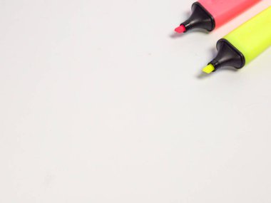 Biri pembe diğeri sarı olmak üzere iki fosforlu kalem beyaz bir arkaplanda köşegen olarak konumlandırılmıştır. Resim, genellikle eğitim ve ofis ortamlarında kullanılan araçları gösteriyor. Kompozisyon, grafik tasarım ve reklamcılık için ideal geniş bir kopya alanı sunuyor., 