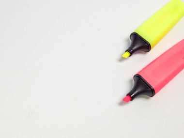 Biri sarı, biri pembe olmak üzere iki renkli fosforlu kalemle yakın plan bir fotoğraf, düz beyaz arka planda dinleniyor. Kompozisyon basit ve temiz, fosforlu kalemler çapraz konumda, görsel ilgi yaratıyor. Görüntü kullanım için ideal