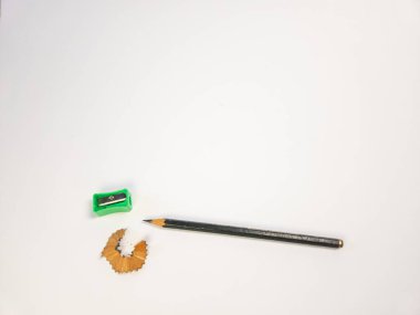 Yukarıdan aşağıya doğru çekimde yeşil bir kalem açacağı, sivri bir kalem ve temiz beyaz zemine karşı ahşap talaşı bulunur. Kompozisyon basit ve düzenlidir, yazı veya çizim için kullanılan araçları vurgular. Resim bir duyuyu iletir