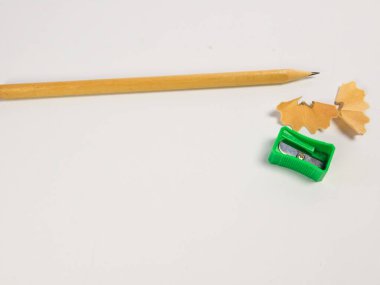 Keskinleştirilmiş bir kalem, yeşil bir kalem açacağı ve düz beyaz bir yüzey üzerinde kalem talaşı gösteren yakın plan bir fotoğraf. Resim, kalem sivri uçlu ve Shar üzerinde odaklanarak, yazı ve çizim için kullanılan araçları vurgular