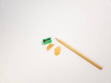 Bir kalem, yeşil bileyici ve talaşlar temiz beyaz arka planda sergilenir. Kompozisyon basit ve minimalist, yazma ve çizim araçlarını vurguluyor. Görüntü, yaratıcılık duygusunu ve bir penisi keskinleştirme sürecini yakalar.