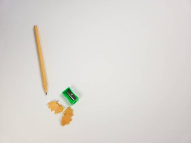 Ahşap bir kalem, yeşil bir kalem açacağı ve sade beyaz arka planda ahşap talaşı içeren basit bir hayat. Resim yukarıdan aşağıya doğru, yazı ve çizim için kullanılan araçları vurguluyor. Kompozisyon temiz ve m