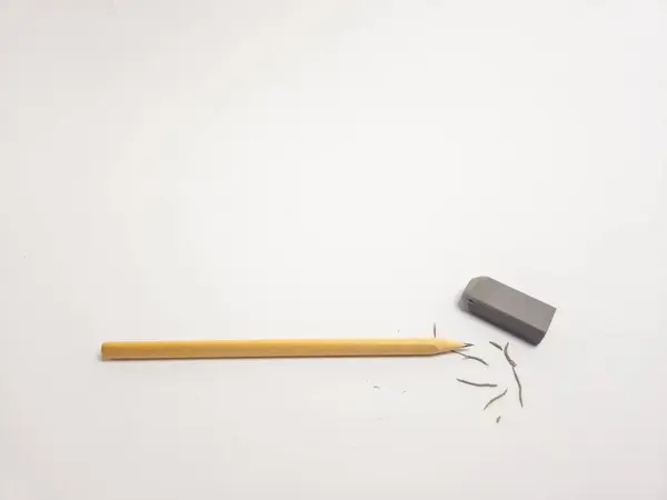 Ahşap bir kalem ve temiz beyaz arka planda gri bir silginin yer aldığı yakın çekim bir stüdyo resmi. Kalemin ucu, yakınlara saçılmış silgi talaşlarıyla kullanım belirtileri gösteriyor. Bu da hataları düzeltme, düzeltme ve düzenleme sürecini sembolize ediyor. Ödeme.