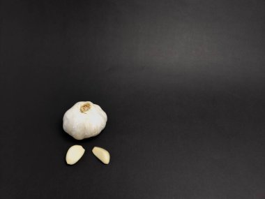 Tam bir sarımsak ampulü ve iki soyulmuş karanfil içeren bir stüdyo çekimi. Kompozisyon sarımsağın dokusunu ve şeklini vurgular, ışık ince gölgeler yaratır. Bu resim mutfak projeleri için idealdir, 