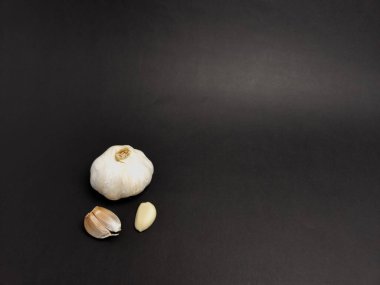 Bir stüdyo çekiminde, koyu siyah arka planda iki karanfil ile birlikte koca bir sarımsak ampulü bulunur. Görüntü, sarımsak derisinin dokusunu ve karanfillerini vurguluyor. Malzemenin taze ve doğal özelliklerini vurguluyor. 