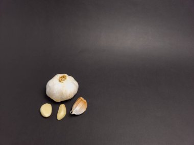 Bir stüdyo çekiminde bütün bir sarımsak ampulü ve koyu gri arka planda üç ayrı karanfil vardı. Işıklandırma sarımsağın dokusunu ve detaylarını vurguluyor. Görüntü temiz ve basit, garl 'ın doğal formu ve tazeliği üzerine odaklanmış.