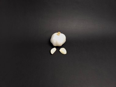 Siyah arka planda iki karanfil bulunan sarımsaklı bir ampulün yakın plan çekimi. Sarımsak beyaz, kahverengi saplı, karanfil pürüzsüz ve kremalı. Kompozisyon minimalisttir ve sarımsağın dokusuna ve şekline odaklanır. Lig.