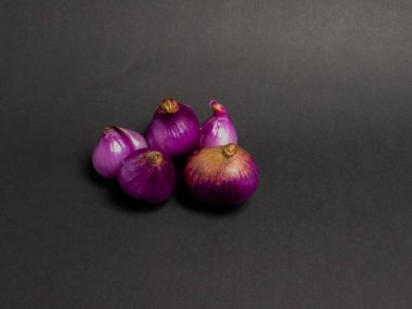 Sade ve koyu arkaplan üzerine dizilmiş canlı kırmızı soğan koleksiyonunun yakın plan çekimi. Bu taze soğanlar yemek pişirmede kullanılmaya hazır basit ve temiz bir kompozisyon sunuyorlar. Görüntü sebzelerin dokusunu ve rengini vurguluyor.