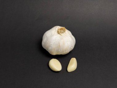 Sarımsaklı bir ampulün yakın çekim stüdyosu ve sade siyah bir arka planda izole edilmiş iki karanfil. Sarımsak beyaz, desenli, karanfil pürüzsüz ve kremalı. Kompozisyon taze, ham maddeleri vurguluyor, yemek pişirmek için mükemmel.