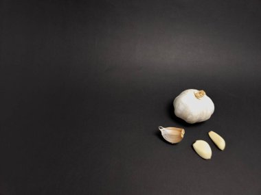 Karanlık bir yüzeye dizilmiş sarımsaklı bir ampulün ve soyulmuş karanfillerin yer aldığı durgun bir yaşam görüntüsü, minimalist ve modern bir kompozisyon yaratır. Işıklandırma yumuşak, sarımsağın dokusunu ve detaylarını vurguluyor. Kompozisyon basit., 