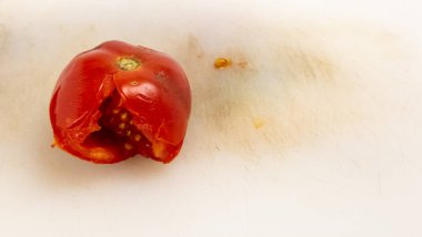 Kırmızı bir domatesin yakın plan çekimi tohumlarını ve etini ortaya çıkarıyor. Domates, üzerinde bıçak izleri olan beyaz bir kesme tahtasının üzerinde duruyor. Görüntü domatesin dokusunun dokusunu ve rengini vurguluyor, tazelik ve doğal besin hissi yaratıyor. Şey... 