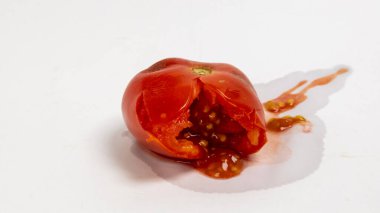 Olgun, kırmızı bir domatesin, tohumlarını ve posasını ortaya çıkaran büyük bir bölünmeyle yakın plan çekimi. Domates, üzerine biraz meyve suyu ve tohum dökülmüş temiz, beyaz bir yüzeye yerleştirilir. Işıklandırma parlak, meyvenin dokusunu ve rengini vurguluyor.