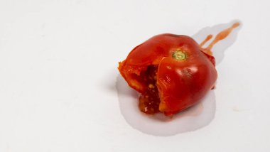 Bu görüntü olgun, ezilmiş kırmızı bir domatesin yakın çekimini yakalar ve hamurlu iç yüzünü ve tohumlarını ortaya çıkarır. Domates suyu beyaz yüzeye sıçramış ve görsel bir kontrast oluşturmuş. Işıklandırma, dokunun ve renginin altını çizer