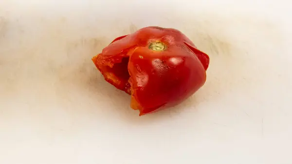 Canlı kırmızı bir domatesin yakın plan çekimi. İçinin sulu olduğunu ortaya çıkarıyor. Domates beyaz bir kesim tahtasının üzerinde duruyor, ürünün dokusunun dokusunu ve tazeliğini gösteriyor. Görüntü domatesin doğal güzelliğini ve detaylarını vurguluyor. 