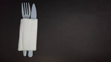 Tepeden tırnağa sergilenen bir fotoğraf seti sarılı bir çatal bıçak takımı. Katlanmış beyaz bir peçetenin içine bir çatal ve bıçak yerleştirilir. Bu aletler muhtemelen plastik. Kurulum koyu, koyu siyah bir yüzeyde. Yemek, yemek servisi veya basit sunum kavramları için ideal.