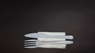 Koyu bir yüzeye yerleştirilmiş plastik çatal, bıçak ve peçete. Çatal bıçak takımı açık mavi ve peçete beyaz. Kompozisyon basit ve minimalisttir, nesnelere odaklanır ve renkler arasındaki kontrasttır. Foo için harika.