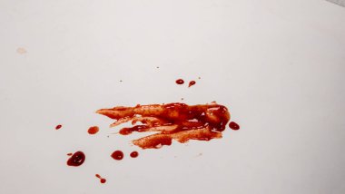 Kırmızı dökülmüş madde, reçel ya da sos içeren beyaz bir yüzeyin yukarıdan aşağı görüntüsü görsel olarak ilginç bir karmaşa yaratır. Resim çeşitli boyutlarda damlalar ve daha büyük bir leke içeriyor. Aydınlatma bile, temiz, minimalist bir estetik yaratıyor.