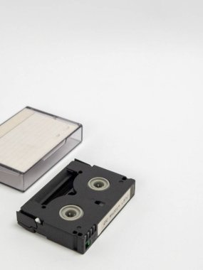 MiniDV kasetinin yakın plan çekimi ve dosyasının temiz beyaz bir arkaplanla karşılaştırılması. Bu resim, MiniDV formatının geçmişe dönük teknolojisini vurguluyor, nostaljiyi çağrıştırıyor ve anıların korunmasını sağlıyor. Konuyla ilgili projeler için uygun