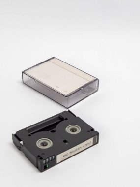 MiniDV kaseti ve şeffaf koruyucu kılıfının yer aldığı bir stüdyo resmi. Kaset siyah ve içinde 