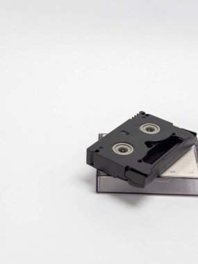 Beyaz bir arkaplan üzerinde duran siyah bir kasetin yakın plan görüntüsü. Görüntü, kasetin ayrıntıları ve dosyasına odaklanarak klasik teknolojiyi ön plana çıkarıyor. Bileşim için yeterli kopyalama alanı sunar 