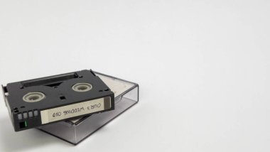 Yakın plan çekimde, temiz plastik kutusunun üzerinde duran bir miniDV kaset yer alıyor. Kasette 