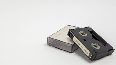 Temiz beyaz bir yüzey üzerinde şeffaf plastik çantasıyla bir MiniDV kaseti sergilenen yakın çekim bir stüdyo resmi. Kaset siyah ve etiketinde 