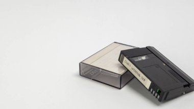 MiniDV kaseti ve beyaz bir yüzey üzerindeki şeffaf plastik kılıfının yakın çekim görüntüsü. Kasette 