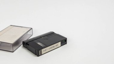 Beyaz bir arkaplanda, yanında açık plastik bir çanta bulunan mini bir kamera bandı bulunuyor. Kasette 