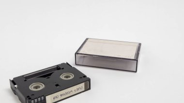 Bir MiniDV kasetinin yakın plan çekimi ve düz beyaz arka planda duran şeffaf plastik bir çanta. Kasette 