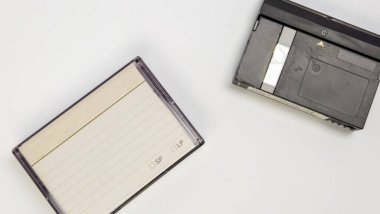 Beyaz arka planda iki klasik video kaseti olan düz bir çekim. Bir kaset standart bir kaset, diğeri ise daha büyük, daha modern bir format. Görüntü, eski teknolojinin nostaljisini ve farklı faktörlerin kontrastını gösteriyor.