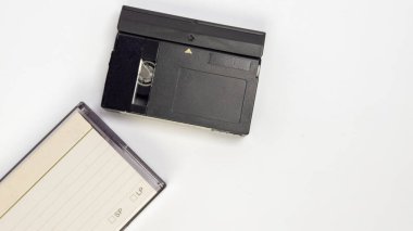 Tepeden çekilen bir karede bir MiniDV bandı ve şeffaf koruyucu kılıfı yer alıyor, her ikisi de temiz beyaz arka planda yer alıyor. MiniDV bandı siyah, tasarımının görünür detaylarıyla birlikte. Koruyucu çantada bilgi kaydetmek için bir etiket var. Bu...