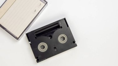 MiniDV video kaseti ve beyaz bir yüzey üzerinde duran şeffaf dosyasının yakın çekim görüntüsü. Siyah kaset, açılışların arasından görünen iki makarayı içerideki kaseti sergiliyor. Çanta, açılır ve yan açılır, bir el yazısı etiketi gösterir