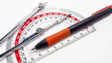 Beyaz bir yüzeye yerleştirilmiş çeşitli geometri aletlerinin yakın çekim stüdyosu. Görüntü bir açıölçer, bir pusula, bir kalem ve bir cetvel içerir. Araçlar çapraz olarak düzenlenir, ilginç bir kompozisyon oluşturur. Aletler yeni ve temiz.