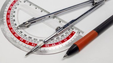 Yakından çekilmiş bir fotoğrafta açıölçer, pusula ve beyaz zemin üzerine dizilmiş bir kalem sergileniyor. Resim araçların detaylarını vurguluyor, tasarımlarını ve işlevselliklerini vurguluyor. Bileşimi temiz ve basit, geometriğe odaklı.