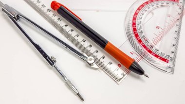 Yakın çekim, beyaz bir yüzeyde düzenlenmiş geometri araçlarının bir koleksiyonunu gösterir. Kompozisyonda bir pusula, bir cetvel, bir açıölçer ve bir kalem yer alıyor. Araçlar çeşitli açılarda konumlandırılmış, ilginç bir düzenleme yaratıyor. Görüntü... 