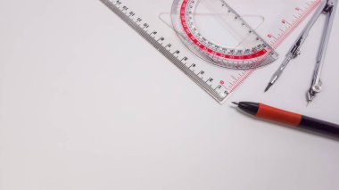 Okul malzemeleri koleksiyonu, içinde üçgen cetvel, açıölçer, pusula ve kalem olan temiz beyaz bir arkaplanda düzenlenmiş. Bu resim eğitim materyalleri, tasarım projeleri veya temiz, organize ve yaratıcı bir görsel ihtiyaç için uygundur.