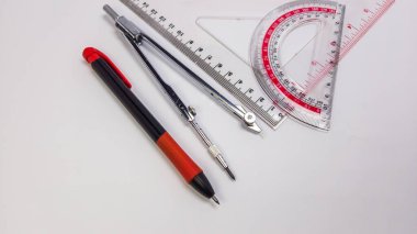 Temiz beyaz bir yüzeye yerleştirilmiş pusula, iletki, cetvel ve kalem gibi geometri araçlarının bir koleksiyonu. Aletler düzgün bir şekilde düzenlenmiş, hassasiyet ve doğruluğa odaklandığını gösteriyor. Resim iyi ışıklandırılmış, araçların ayrıntılarını vurguluyor