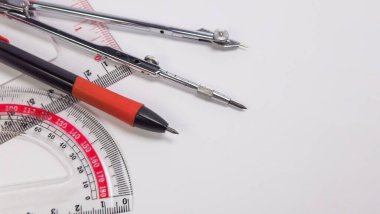 Yakın çekim, beyaz arkaplanda taslak araçların bir derlemesini sunar. Kompozisyon bir pusula, bir açıölçer ve bir kalem içerir, hepsi görsel olarak çekici ve bilgilendirici bir sahne yaratmak için düzenlenmiştir. Araçlar belli bir açıyla yerleştirilmiş, wi