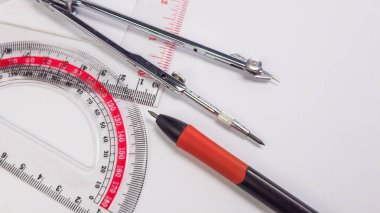 Beyaz bir yüzeye yerleştirilmiş çeşitli çizim araçlarının yakın çekim görüntüleri. Görüntü bir açıölçer, bir pusula, bir cetvel ve bir mekanik kalem gösteriyor. Araçlar şekillerini ve biçimlerini vurgulayacak şekilde yerleştirilmiş. Bu resim için uygundur 
