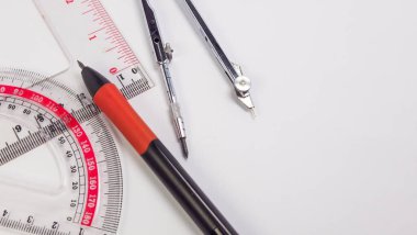Temiz beyaz bir yüzeye yerleştirilmiş iletki, cetvel ve pusula gibi temel geometri araçlarını içeren yakın plan bir çekim. Resim geometride kullanılan araçları gösterir, eğitim materyalleri için mükemmel, matematiksel kavramları gösteren, bir