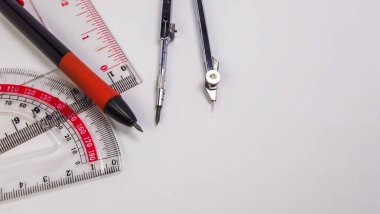 Temiz, beyaz bir arkaplanda düzenlenmiş açıölçer, cetvel ve pusula da dahil olmak üzere geometri araçlarının bir koleksiyonunu gösteren bir tepeden çekim. Resim araçların ayrıntılarını vurgular ve eğitim ve eğitim için uygun basit ve temiz bir bileşim oluşturur 