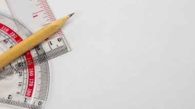 Bu resim, beyaz arka planda okul malzemelerinin yakın çekimini içeriyor. Tahta bir kalem, temiz bir plastik cetvel ve kalemin ucu sağ üst tarafı işaret eden bir açıölçer boyunca uzanır. Kompozisyon temiz ve basit, Su.